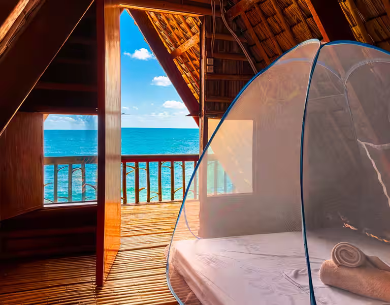 Chambre avec moustiquaire et vue sur l’océan dans le bungalow de plage à L’Astrolabe Ecolodge